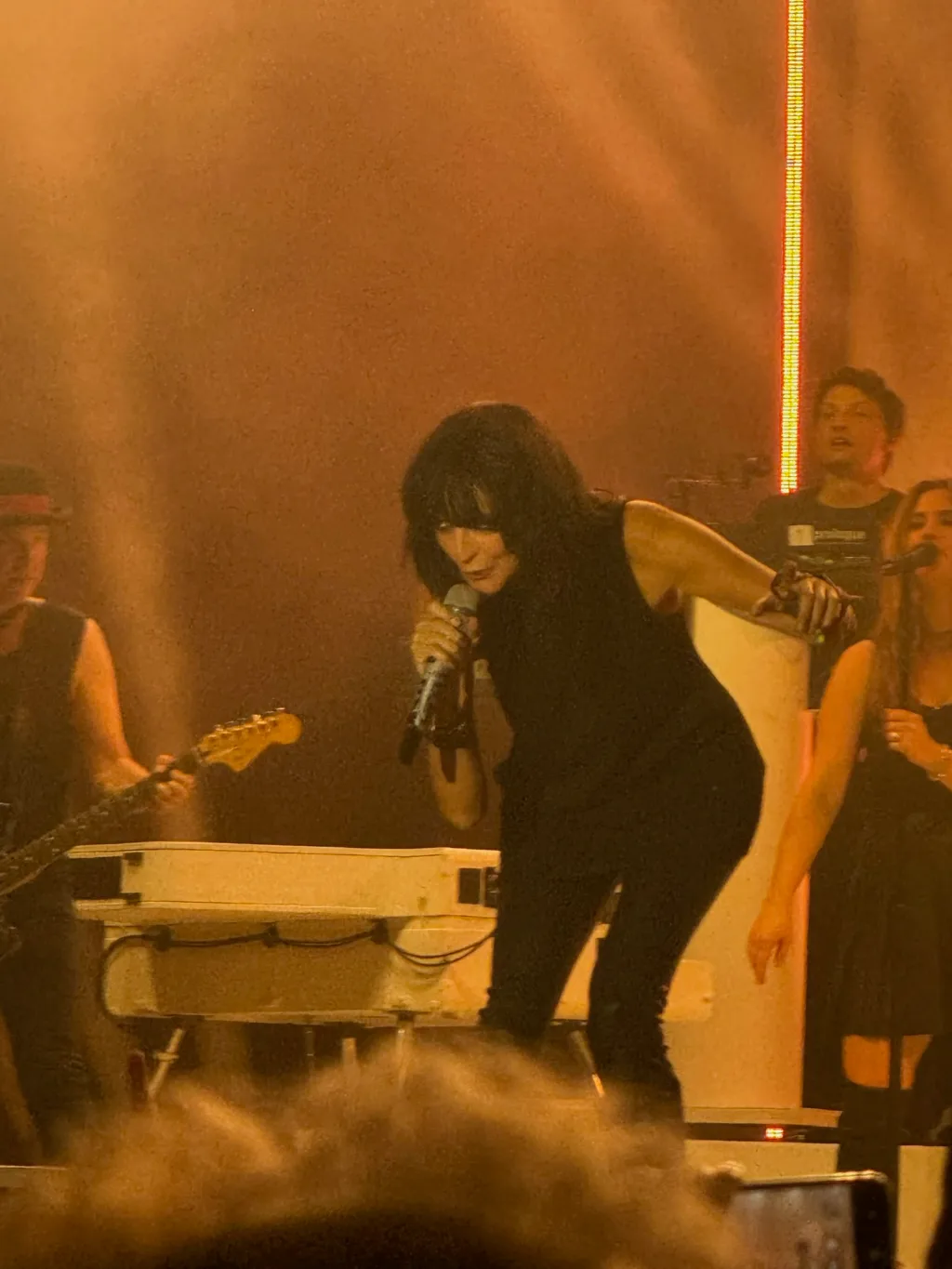 Nena in Schwarz singt vorgebeugt ins Mikrofon auf einer orange beleuchteten Bühne, neben ihr die Band.