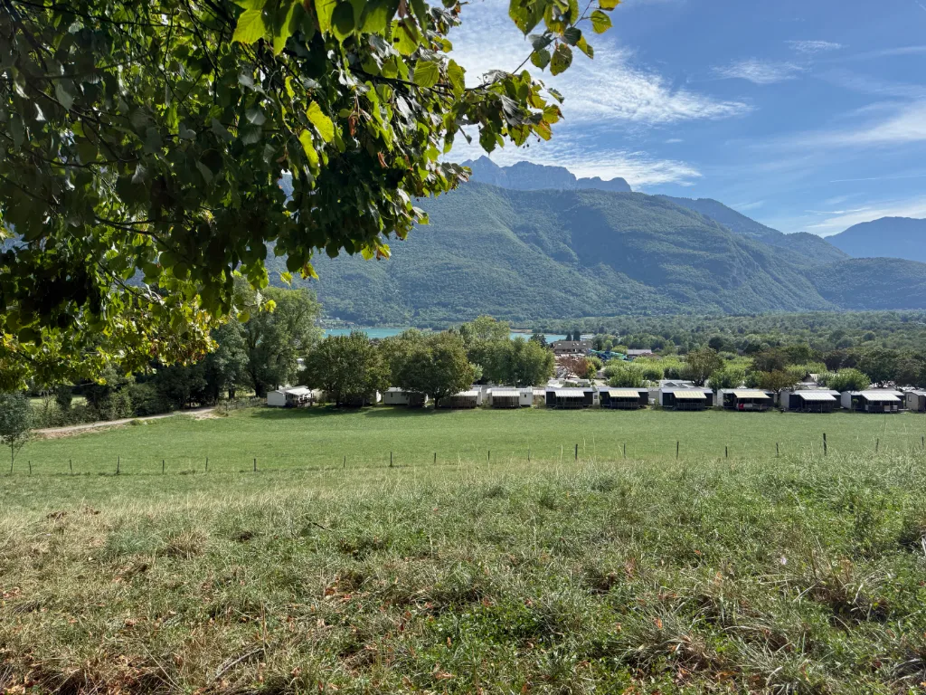 Blick über eine Wiese auf eine Reihe von Mobilheimen, dahinter ein türkiser See und bewaldete Berge.