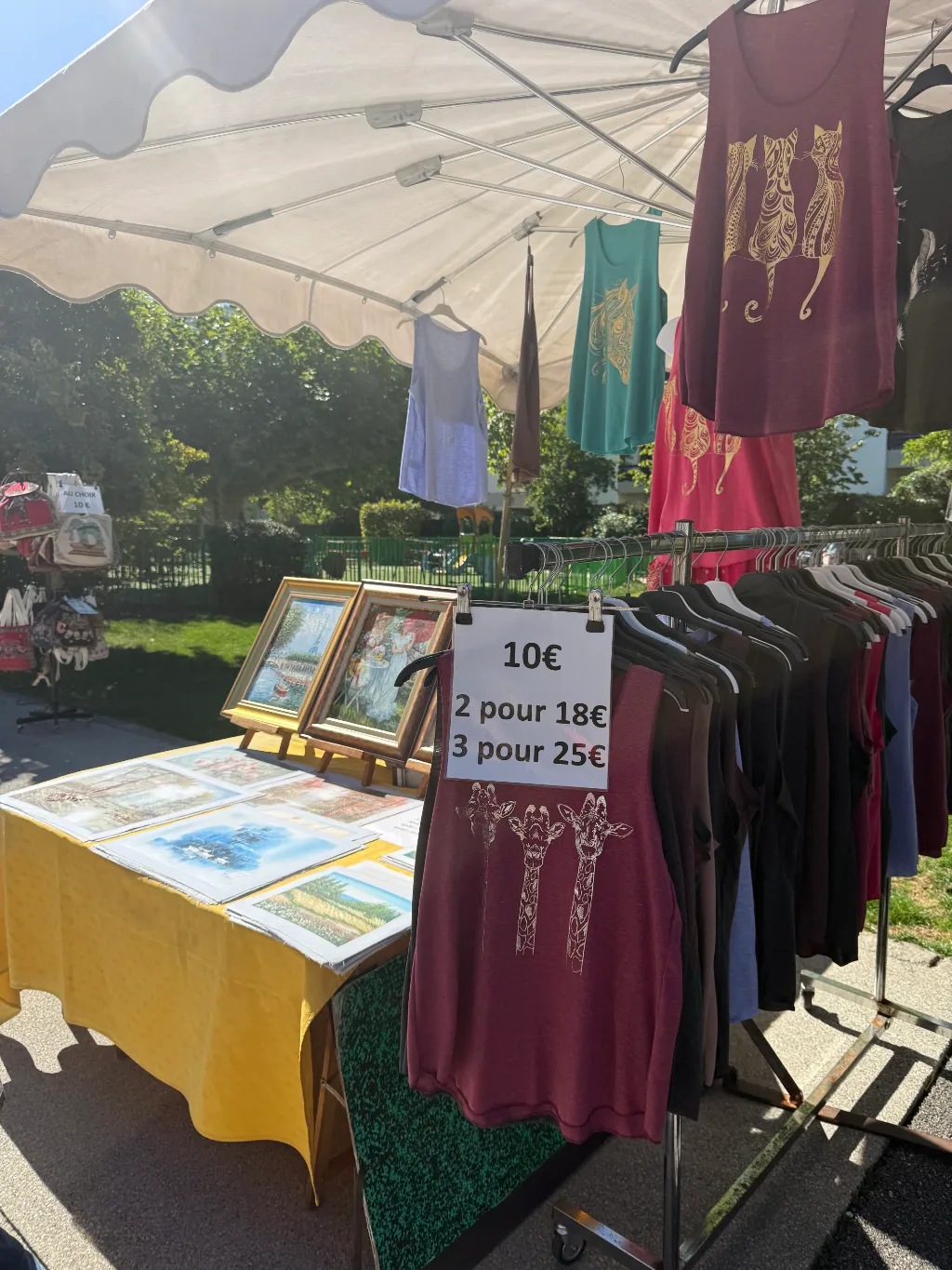 Marktstand mit bedruckten Trägertops auf Kleiderstange und Bildern, Schild „10€, 2 pour 18€, 3 pour 25€“.