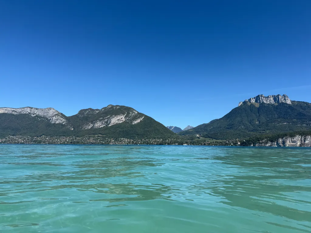Türkisgrüner Bergsee mit bewaldeten Felsbergen am Ufer unter wolkenlosem blauem Himmel.